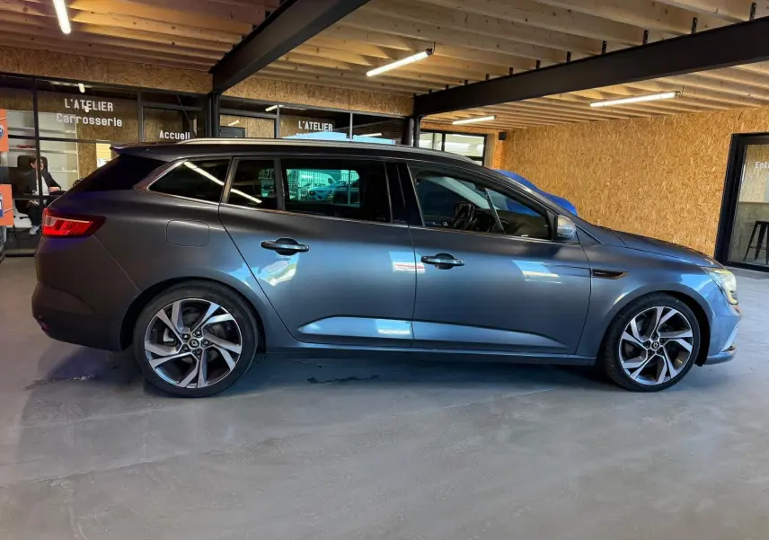 Profil droit d’une Renault Mégane Break GT gris métallisé, stationnée en intérieur avec jantes alliage distinctives.