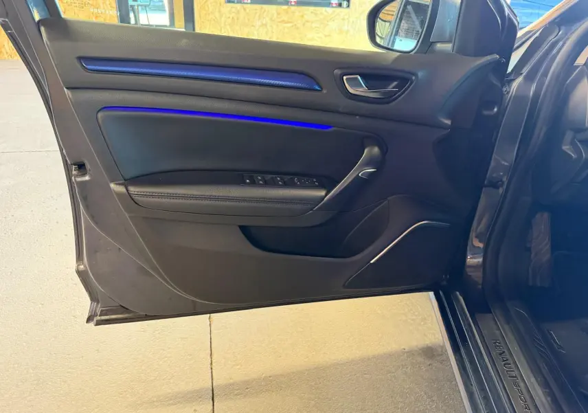 Vue rapprochée de la porte avant gauche ouverte d’une Renault Mégane Break GT grise, avec éclairage d’ambiance bleu sur la garniture.
