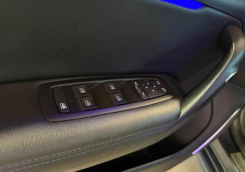 Gros plan sur la commande des vitres électriques côté conducteur de la Renault Mégane Break gris, intérieur cuir noir.