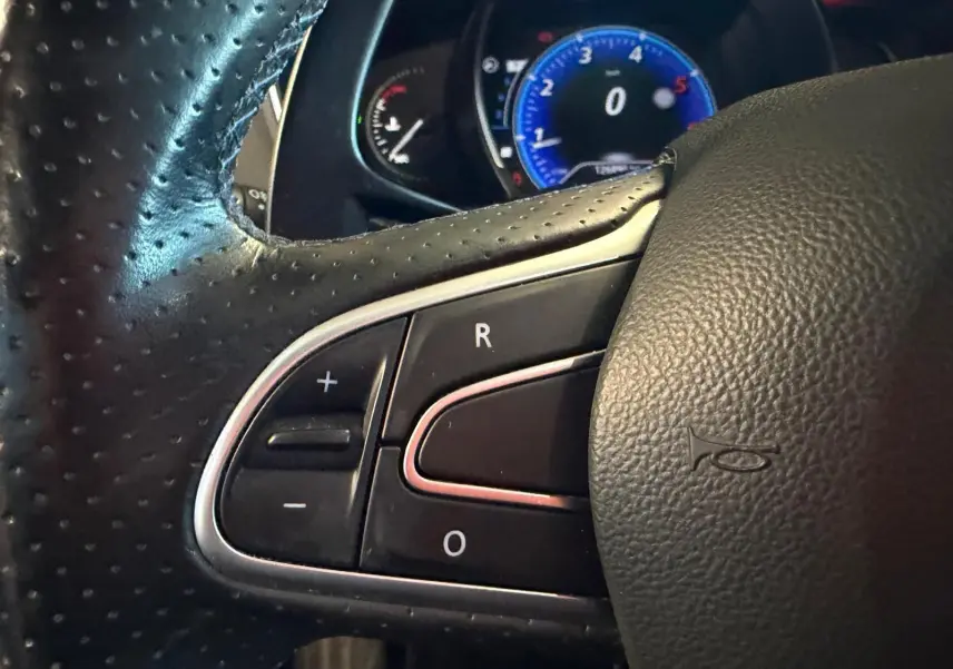 Gros plan sur le volant en cuir noir de la Renault Mégane Break GT 2017, avec commandes intégrées et tableau de bord bleu en arrière-plan.