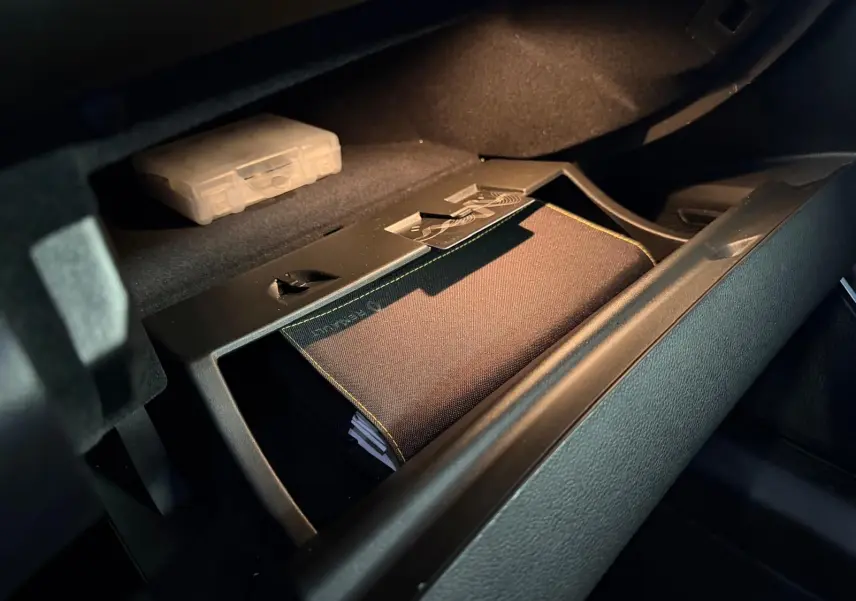 Vue rapprochée de la boîte à gants ouverte du Renault Mégane Break GT gris, avec un manuel de bord visible à l'intérieur.