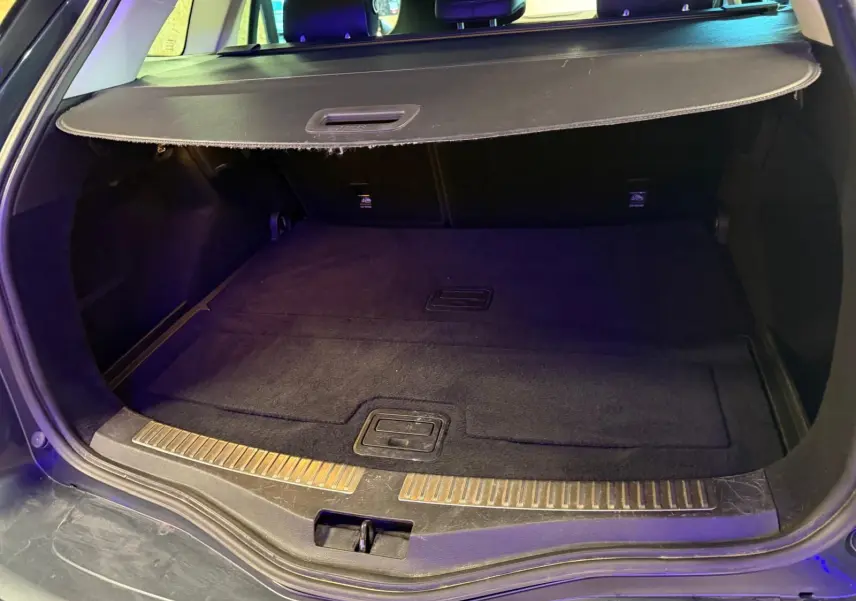 Coffre ouvert vu de l'arrière d'une Renault Mégane Break gris, avec cache-bagages et tapis noir.