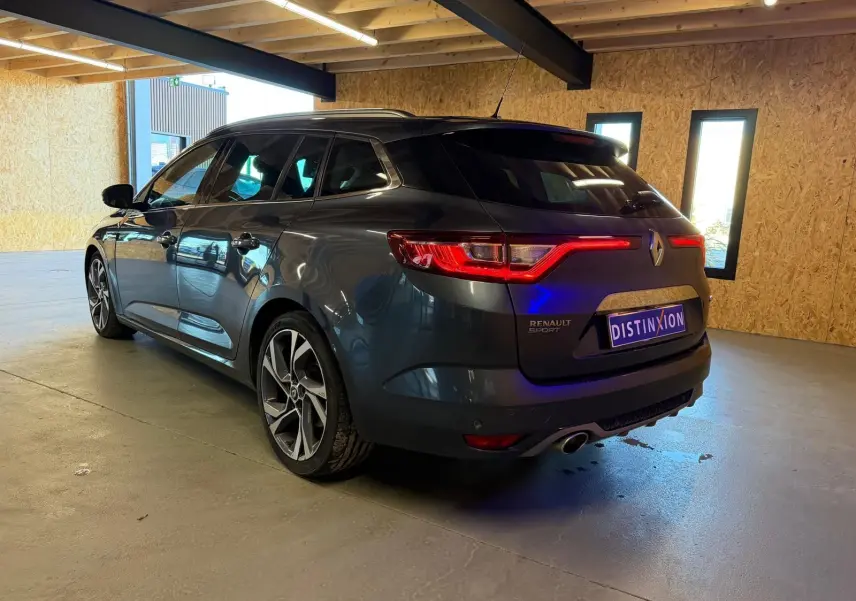 Renault Mégane Break GT gris vue 3/4 arrière droit en intérieur, feux arrière allumés et jantes sport visibles.