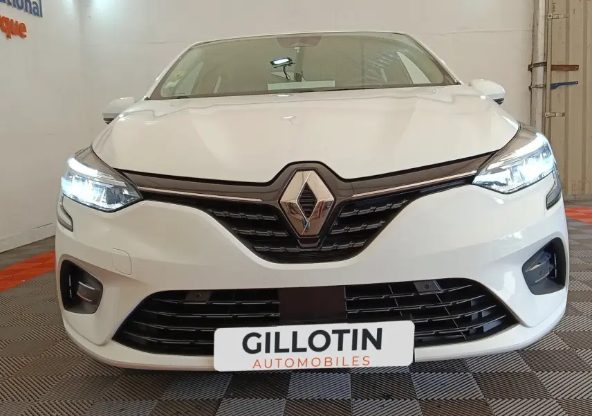Vue avant d'une Renault Clio Business Blue dCi 100 blanche avec phares LED allumés dans un showroom.
