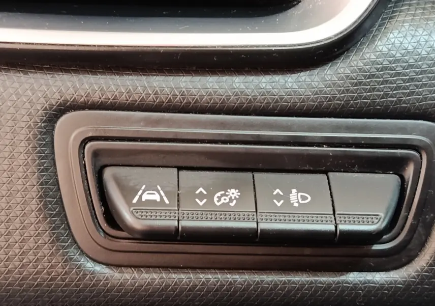Gros plan sur les boutons de réglage d'assistance et phares du tableau de bord noir de la Renault Clio Business Blue dCi 100 blanche.
