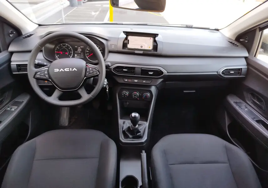 Vue intérieure avant du tableau de bord noir et volant DACIA avec boîte manuelle, sièges tissu gris foncé dans une Sandero blanche.
