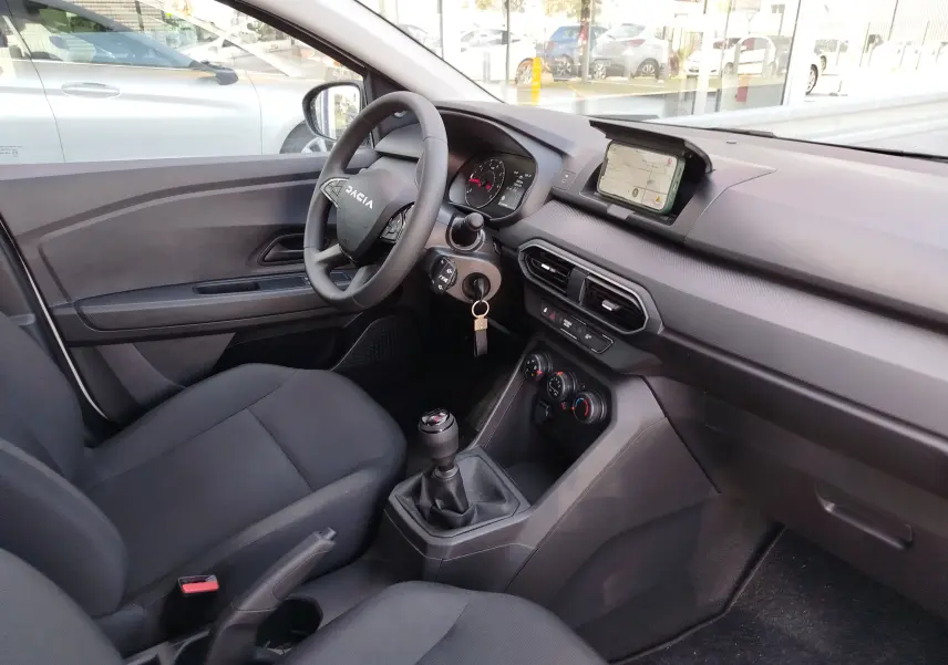 Intérieur de la Dacia Sandero 2025 vu côté conducteur, tableau de bord gris avec écran tactile et boîte manuelle.