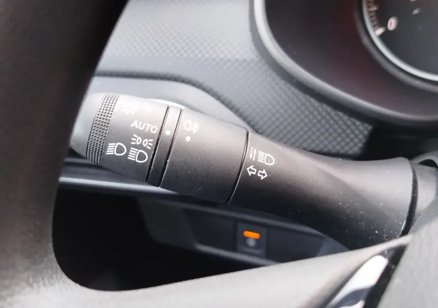 Gros plan sur la commande des feux et clignotants à gauche du volant dans le tableau de bord gris d'une Dacia Sandero blanche.