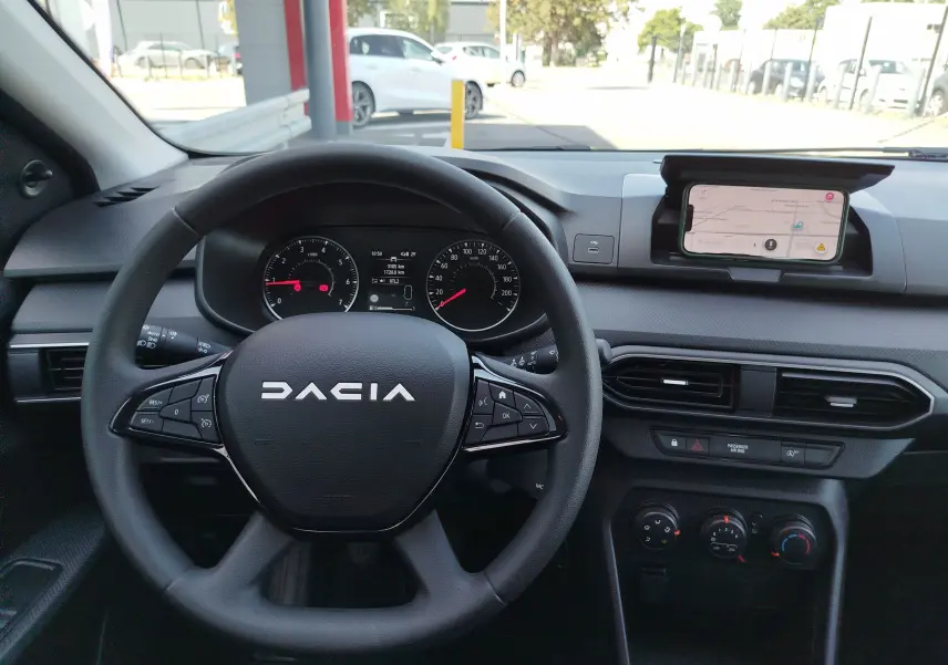 Vue intérieure centrée sur le volant noir de la Dacia Sandero 2025, avec tableau de bord et écran smartphone en mode navigation.