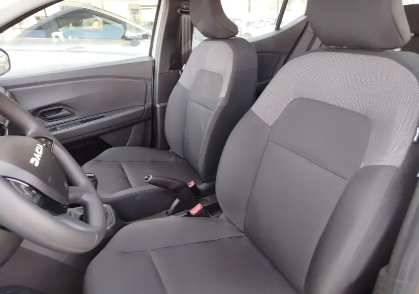 Vue intérieure côté avant gauche de la Dacia Sandero 2025, sièges tissu gris foncé avec volant multifonction.