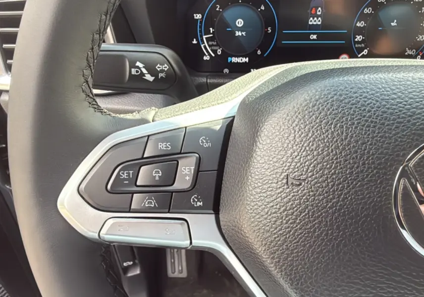 Gros plan sur le volant cuir noir du Volkswagen Amarok 2025, avec commandes de régulateur de vitesse et tableau de bord numérique.