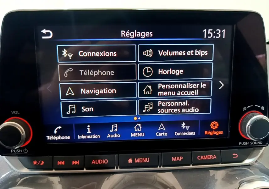 Écran tactile central du Nissan Juke Hybrid 2023 affichant le menu Réglages avec boutons audio et caméra.