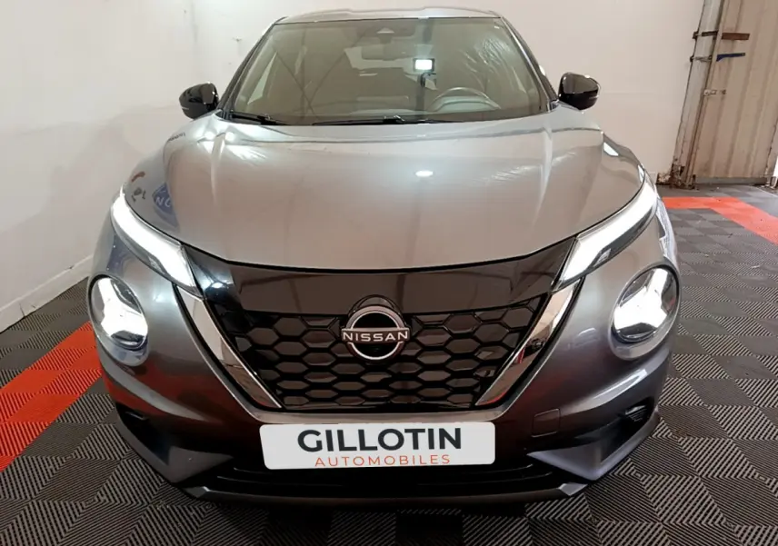 Vue frontale d'un Nissan Juke Hybrid 143 Business+ gris foncé avec phares LED allumés et calandre noire hexagonale.