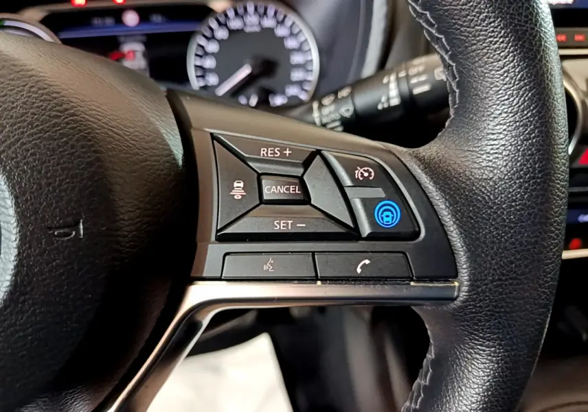 Gros plan sur les commandes du volant cuir noir du Nissan Juke Hybrid 143 Business+ 2023 avec affichage du tableau de bord flou.