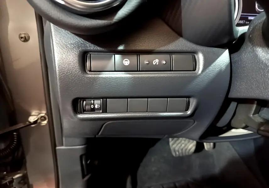 Gros plan sur les commandes de réglage de luminosité et assistance au volant côté gauche du tableau de bord du Nissan Juke gris foncé.