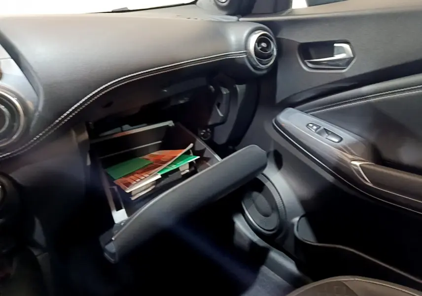 Vue intérieure côté passager du tableau de bord noir avec boîte à gants ouverte contenant des documents dans un Nissan Juke 2023.