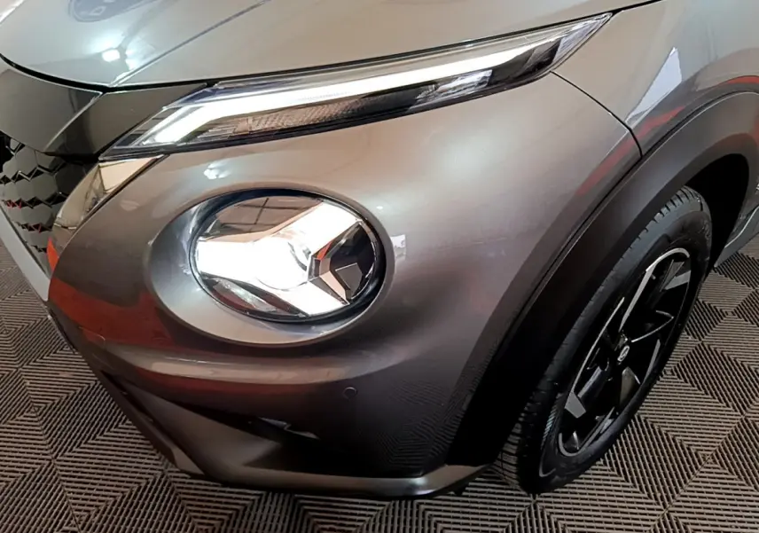 Gros plan sur l'avant droit gris foncé du Nissan Juke Hybrid 143 Business+ avec phare rond et jante noire.