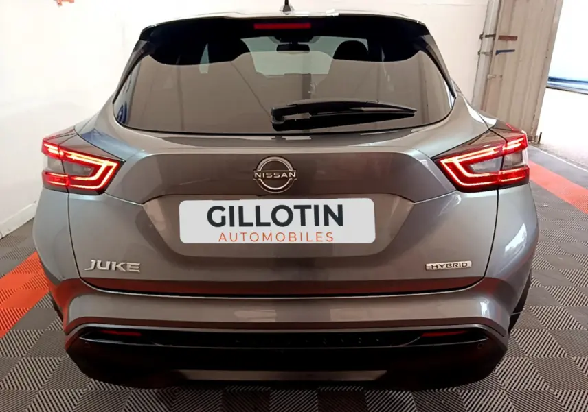 Vue arrière du Nissan Juke Hybrid gris foncé 2023 avec feux LED allumés et logo visible sur un sol damier noir et rouge.