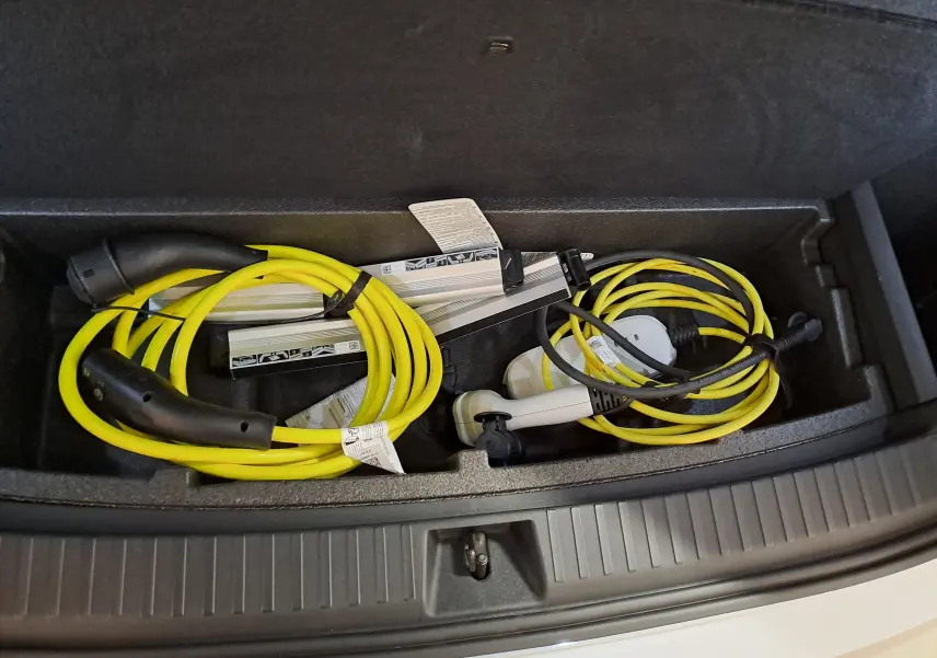 Coffre ouvert d’un Skoda Kodiaq gris argent 2025 montrant les câbles de recharge jaune et blanc rangés dans un compartiment.