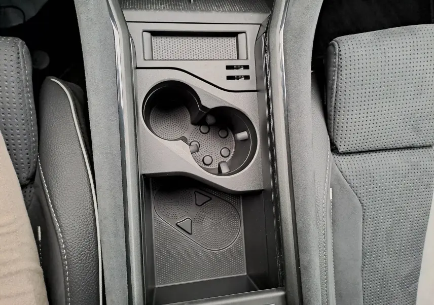 Vue plongeante sur la console centrale noire du Skoda Kodiaq 2025, avec porte-gobelets et rangement entre sièges perforés.