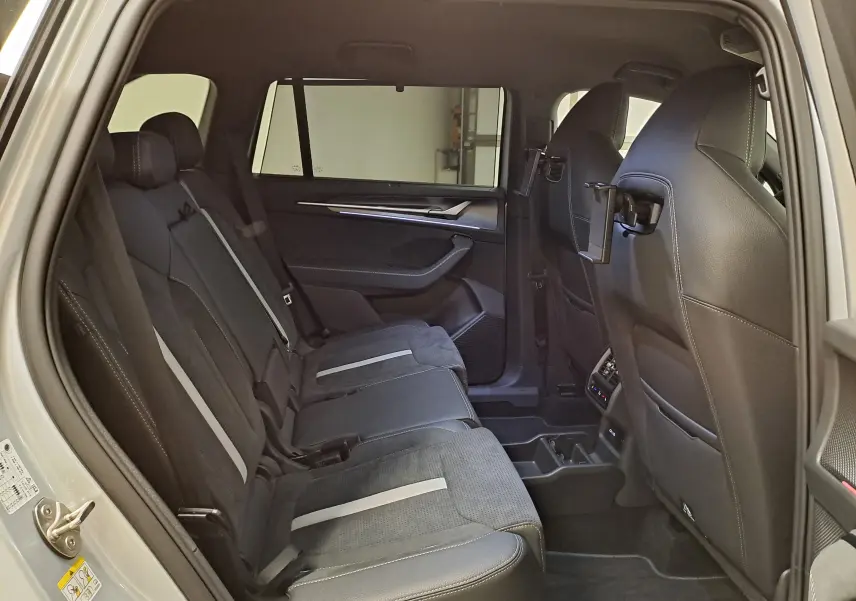 Vue intérieure arrière côté gauche du Skoda Kodiaq gris argent, sièges noirs avec bandes grises et tablettes intégrées aux appuie-têtes avant.