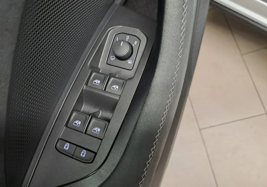 Gros plan sur les commandes de lève-vitres et réglage des rétroviseurs sur la porte côté conducteur d'un Skoda Kodiaq gris argent.