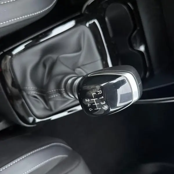 Vue rapprochée du levier de vitesse manuel noir de la Citroën C3 Turbo 100 ch, entouré de sièges gris foncé.