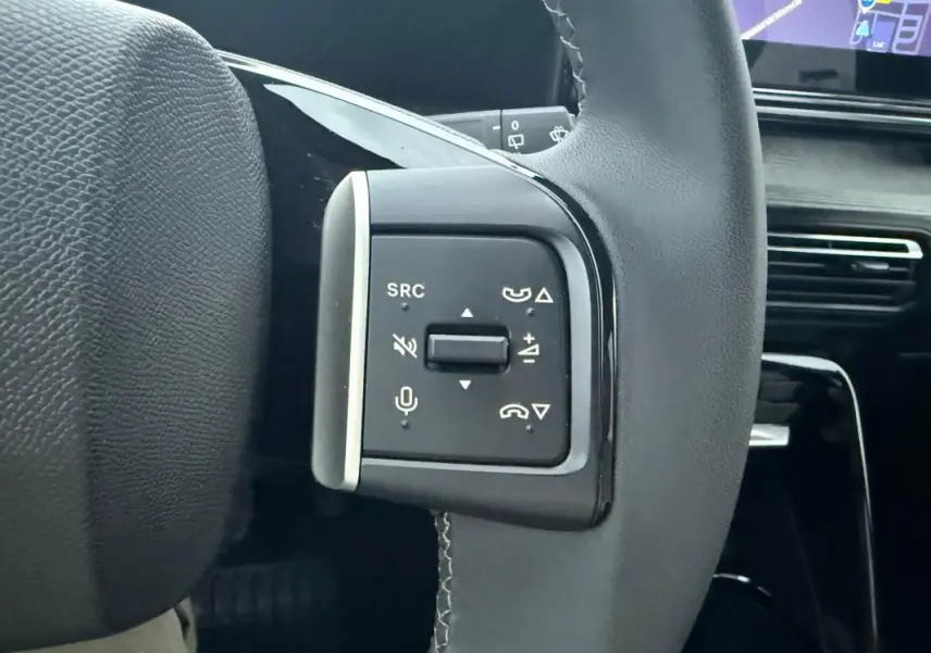 Gros plan sur les commandes multifonctions du volant noir d'une Citroën C3 gris 2025, avec écran tactile en arrière-plan.