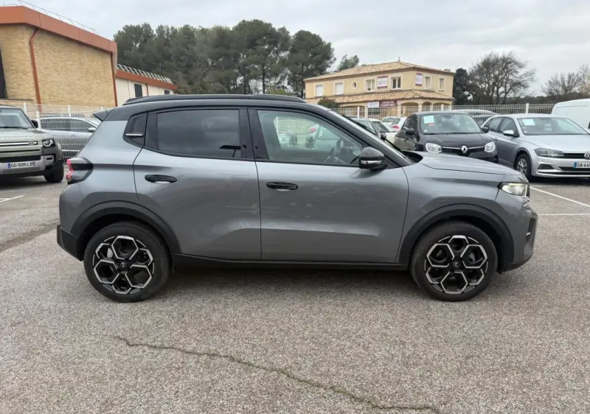 Profil droit d'une Citroën C3 gris 2025 avec jantes alliage noires et toit noir, stationnée en extérieur.