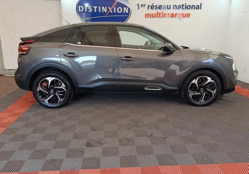 Profil droit d'une Citroën C4 2022 gris foncé avec jantes noires et détails chromés, en intérieur showroom.