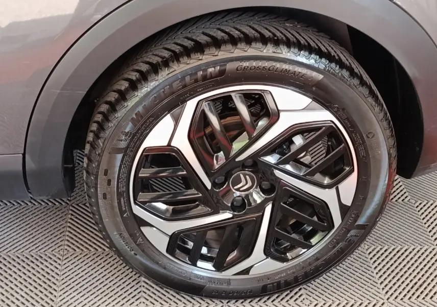 Gros plan sur la roue avant droite d'une Citroën C4 gris foncé, avec jante alliage bicolore et pneu Michelin.