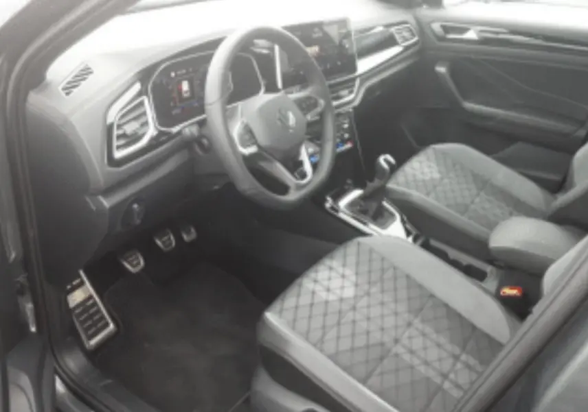 Vue intérieure côté conducteur du Volkswagen T-Roc gris platinium, mettant en valeur le volant multifonction et les sièges en tissu matelassé.