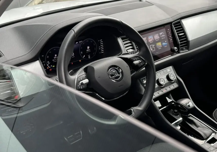 Vue intérieure du poste de conduite du Skoda Kodiaq blanc, mettant en valeur le volant multifonction et l'écran tactile central.