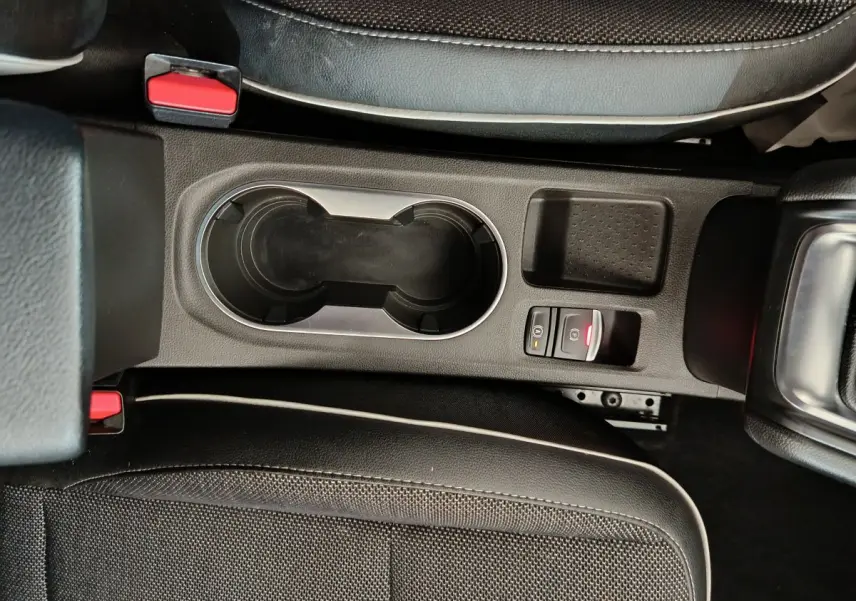Gros plan sur la console centrale noire du Renault Captur gris foncé, avec porte-gobelets et frein à main électrique.