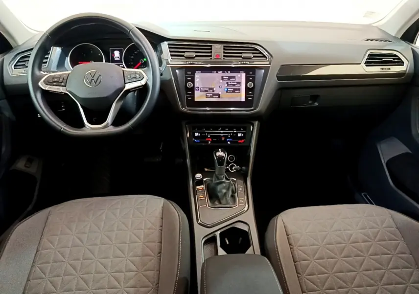 Vue intérieure frontale du tableau de bord et volant cuir noir du Volkswagen Tiguan gris clair 2021 avec écran tactile central.