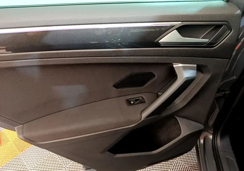 Vue rapprochée de la porte côté gauche du Volkswagen Tiguan 2021, garniture noire avec poignée argentée et haut-parleur intégré.