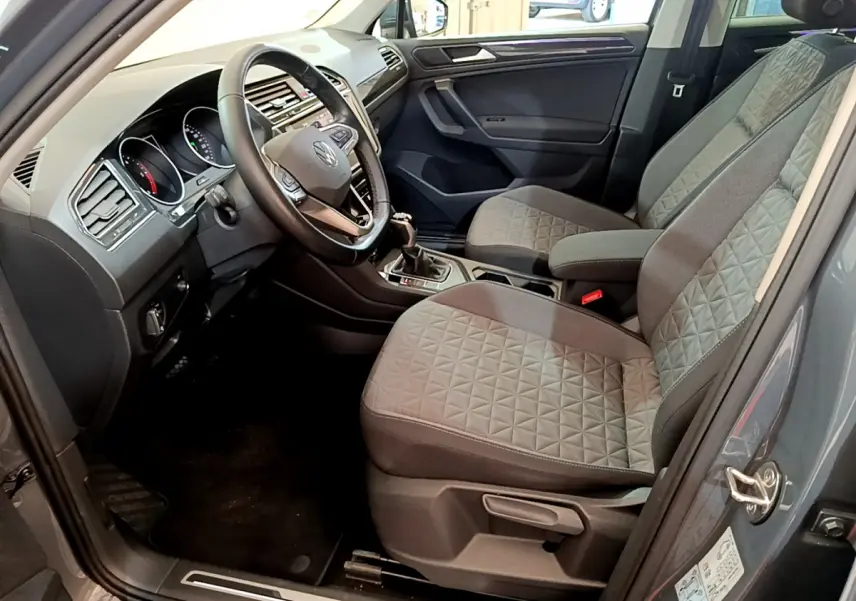 Vue intérieure côté conducteur du Volkswagen Tiguan gris clair 2021, sièges tissu à motifs géométriques et volant cuir multifonctions.