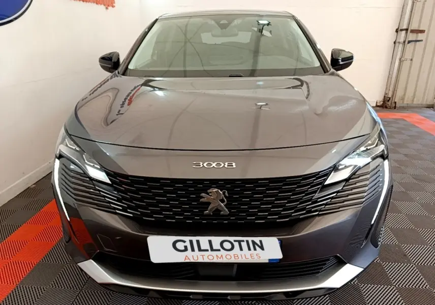 Vue frontale d'un Peugeot 3008 gris foncé avec calandre noire et éclairage LED distinctif en intérieur showroom.