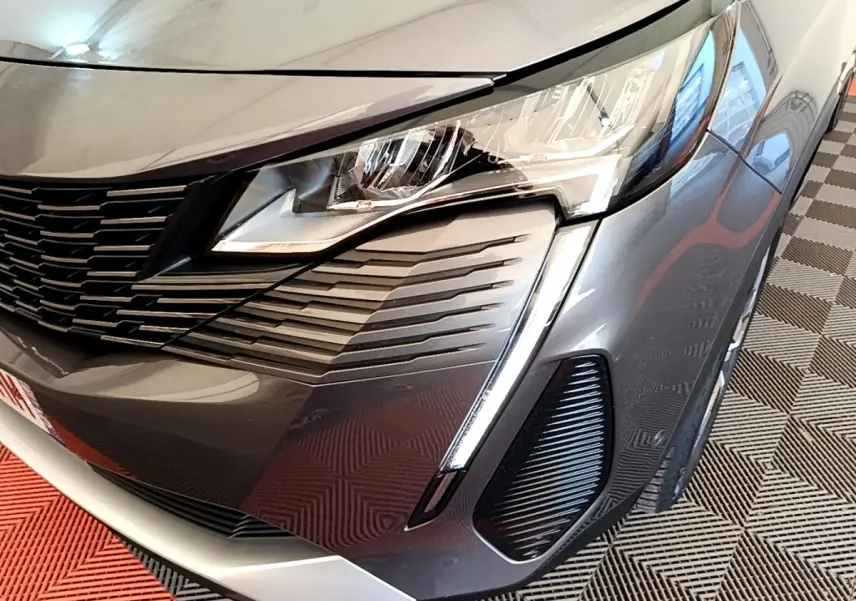 Gros plan sur l'avant droit gris foncé du Peugeot 3008 2022, mettant en valeur le phare et la calandre distinctive.