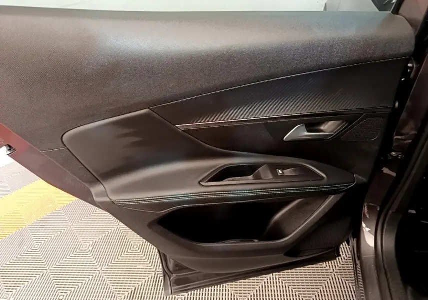 Intérieur de la porte côté gauche du Peugeot 3008 gris foncé, avec garniture noire et insert effet carbone.