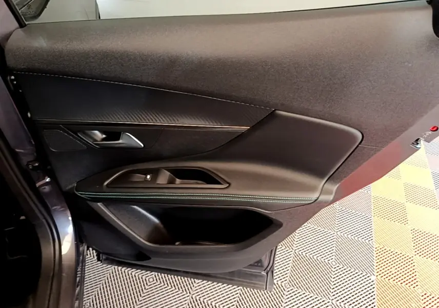 Vue rapprochée de la porte arrière gauche du Peugeot 3008 gris foncé, avec garniture noire et surpiqûres vertes.