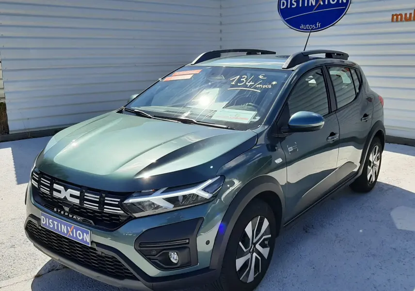 Vue 3/4 avant droite d'une Dacia Sandero Stepway 2025 vert cèdre avec barres de toit et calandre noire distinctive.