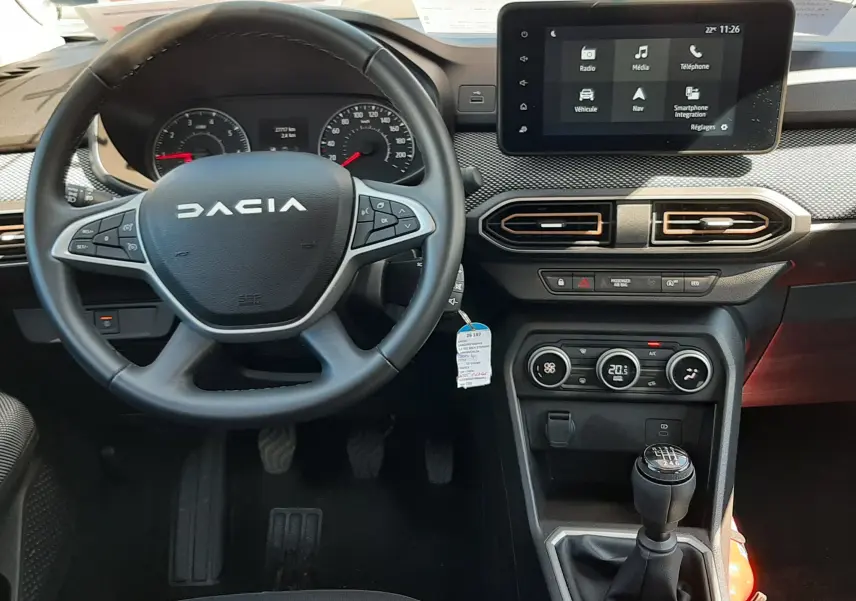 Vue intérieure centrée sur le volant DACIA et la console centrale avec écran tactile et levier de vitesses manuel.