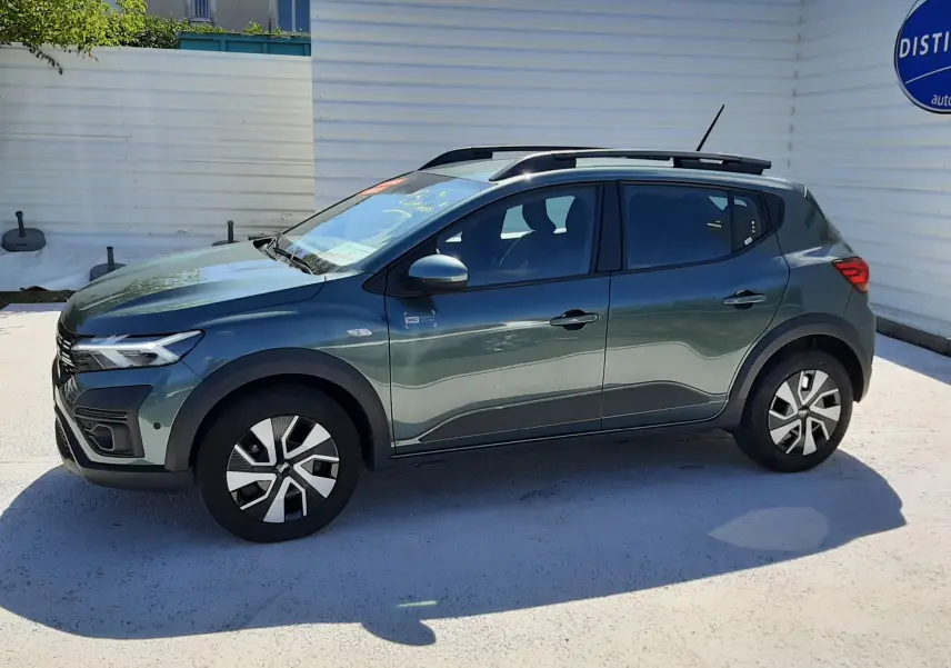 Vue de profil côté gauche d'une Dacia Sandero Stepway 2025 vert cèdre avec barres de toit et jantes distinctives.