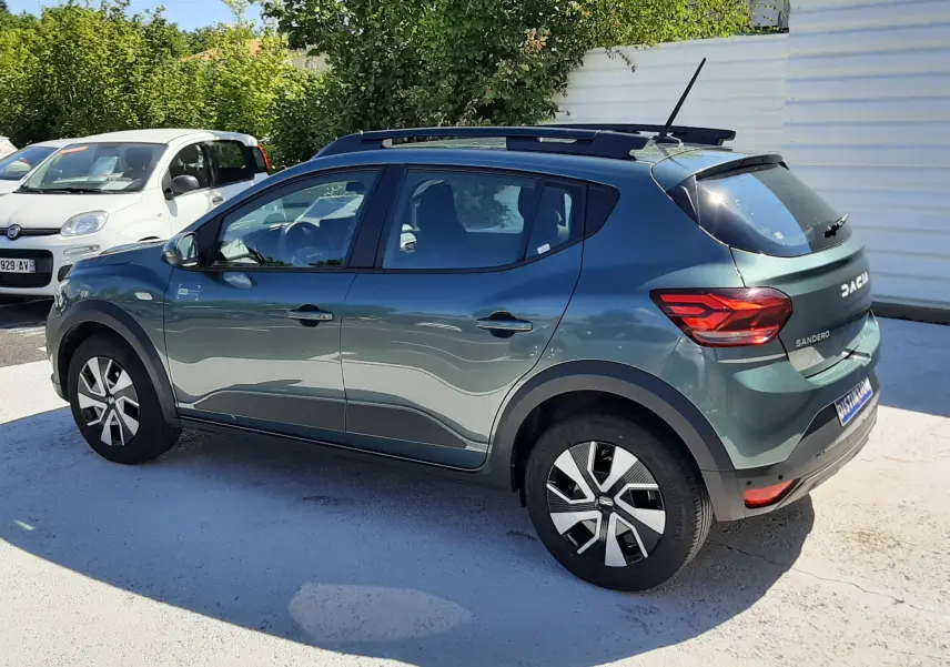 Vue 3/4 arrière droite d'une Dacia Sandero Stepway 2025 en vert cèdre avec barres de toit et jantes distinctives.