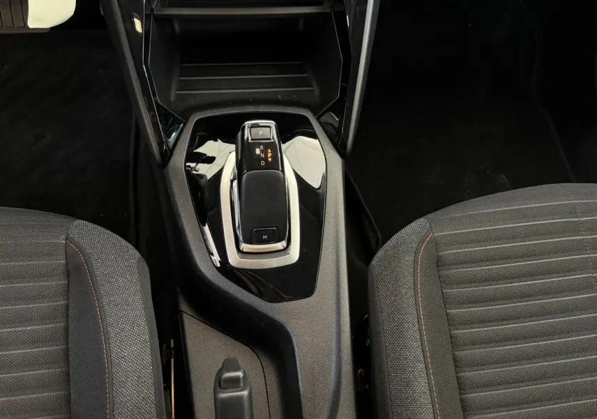 Le levier de vitesse de la Peugeot 208 PureTech noir, vu de dessus entre les sièges avant en tissu gris.