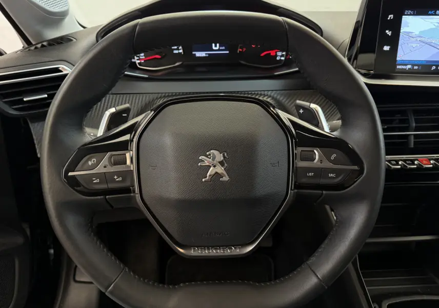 Vue rapprochée du volant cuir noir de la Peugeot 208 2021 avec commandes multifonctions et tableau de bord numérique.