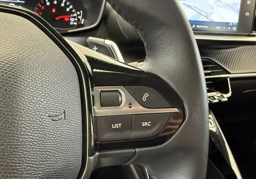 Gros plan sur le volant cuir noir de la Peugeot 208 2021 avec commandes audio et tableau de bord numérique.