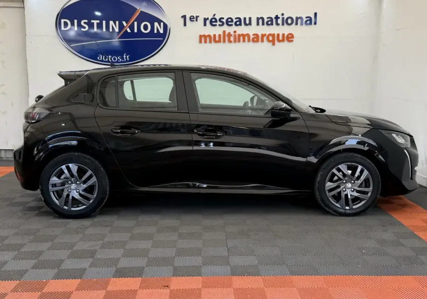 Peugeot 208 noire vue de profil côté gauche, stationnée en intérieur avec jantes alliage et vitres teintées.