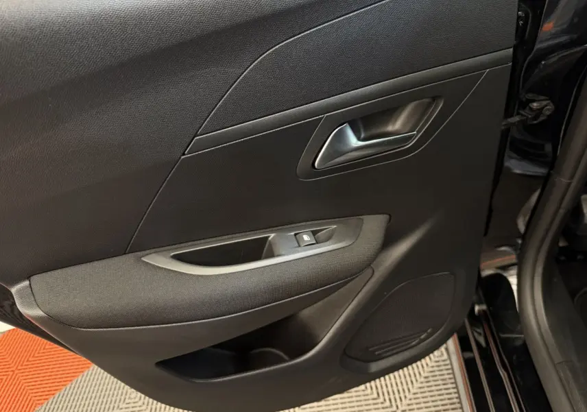 Gros plan sur la porte côté gauche noire de la Peugeot 208 2021, avec poignée argentée et commande de lève-vitre.
